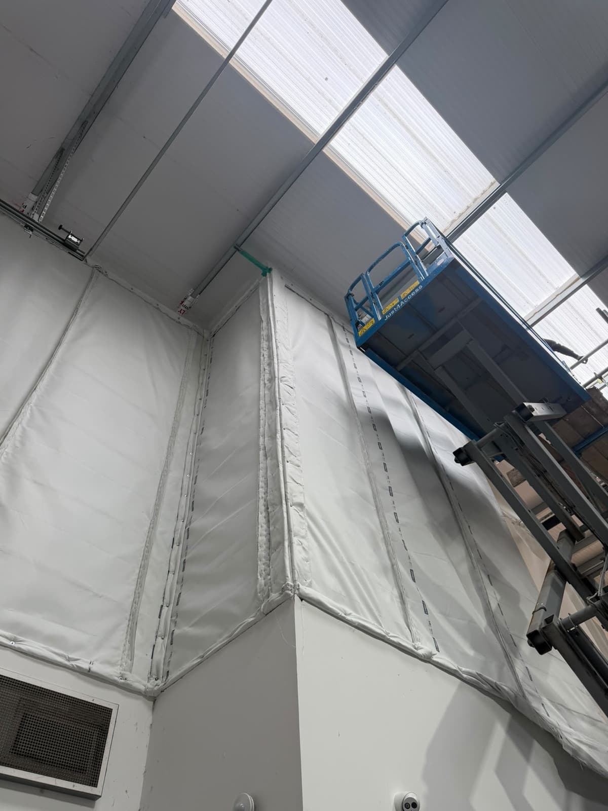 The barrier wrapping the corner of the office block up to the warehouse roof, with the scissor lift alongside